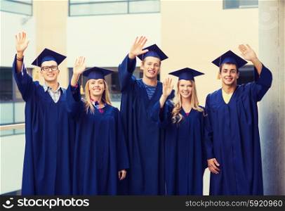 education, graduation and people concept - group of smiling students in mortarboards and gowns waving hands outdoors