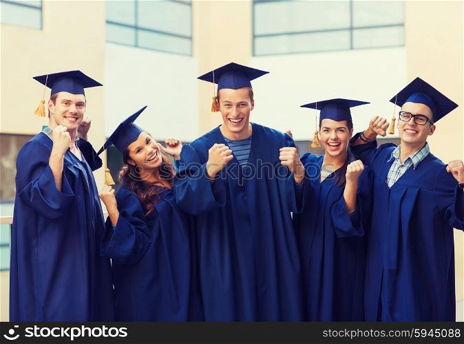 education, graduation and people concept - group of smiling students in mortarboards and gowns making triumph gesture outdoors