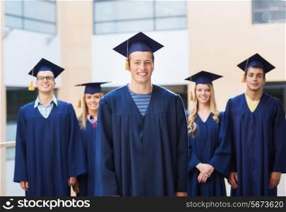 education, graduation and people concept - group of smiling students in mortarboards and gowns outdoors