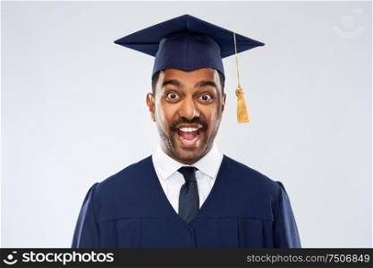 education, graduation and people concept - happy excited indian male graduate student in mortar board and bachelor gown over grey background. happy indian graduate student in mortar board