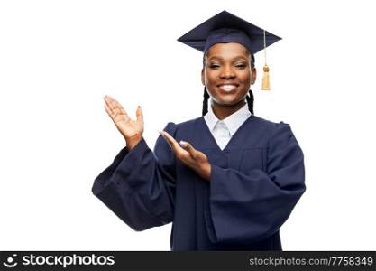 education, graduation and people concept - happy graduate student woman in mortarboard and bachelor gown showing something imaginary over white background. happy female graduate student in mortarboard