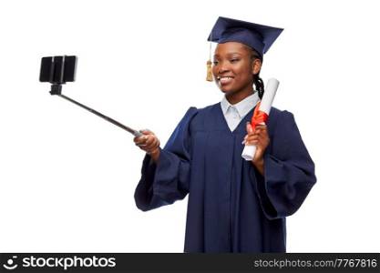 education, graduation and people concept - happy graduate student woman in mortarboard and bachelor gown with diploma and smartphone taking selfie over white background. female graduate student with diploma taking selfie