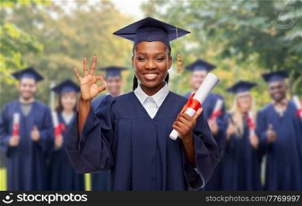 education, graduation and people concept - happy graduate student woman in mortarboard and bachelor gown with diploma showing ok gesture over white background. female graduate student with diploma showing ok