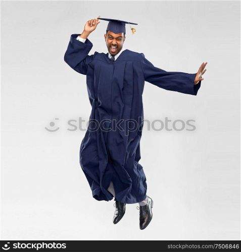 education, graduation and people concept - happy indian male graduate student in mortar board and bachelor gown celebrating success and jumping over grey background. happy male indian graduate student jumping