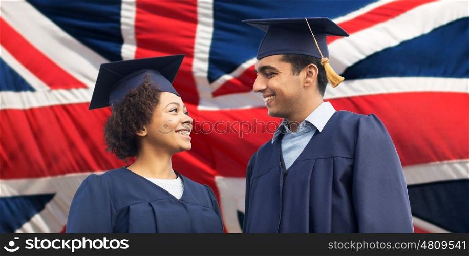 education, graduation and people concept - happy international students in mortar boards and bachelor gowns over british flag background