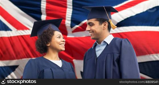 education, graduation and people concept - happy international students in mortar boards and bachelor gowns over british flag background