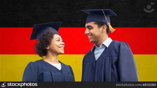 education, graduation and people concept - happy international students in mortar boards and bachelor gowns over german flag background