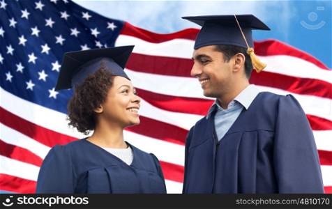 education, graduation and people concept - happy international students in mortar boards and bachelor gowns over american flag background