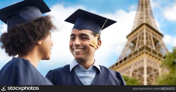 education, graduation and people concept - happy international students in mortar boards and bachelor gowns over eiffel tower background