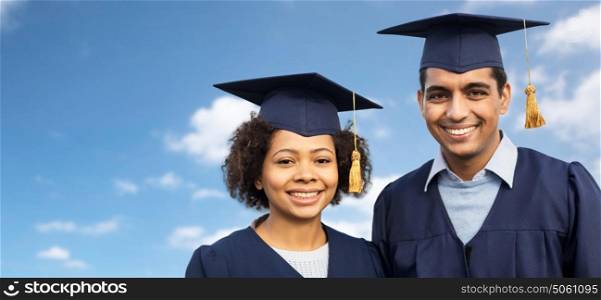 education, graduation and people concept - happy international students in mortar boards and bachelor gowns over blue sky and clouds background. students or bachelors in mortar boards over sky