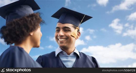 education, graduation and people concept - happy international students in mortar boards and bachelor gowns over blue sky and clouds background. happy students or bachelors over blue sky. happy students or bachelors over blue sky