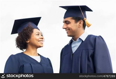 education, graduation and people concept - happy international students in mortar boards and bachelor gowns outdoors