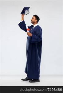 education, graduation and people concept - happy smiling indian male graduate student in mortar board and bachelor gown with diploma celebrating success over grey background. male graduate student in mortar board with diploma