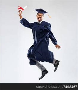 education, graduation and people concept - happy smiling indian male graduate student in mortar board and bachelor gown with diploma celebrating success and jumping over grey background. happy jumping indian graduate student with diploma