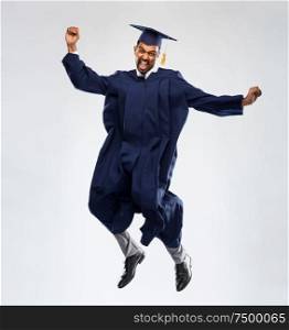 education, graduation and people concept - happy smiling indian male graduate student in mortar board and bachelor gown celebrating success and jumping over grey background. happy male indian graduate student jumping