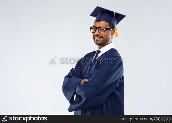 education, graduation and people concept - happy smiling indian male graduate student in mortar board and bachelor gown over grey background. graduate student in mortar board and bachelor gown