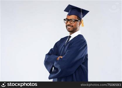 education, graduation and people concept - happy smiling indian male graduate student in mortar board and bachelor gown over grey background. graduate student in mortar board and bachelor gown