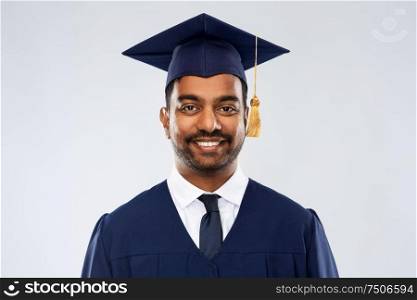 education, graduation and people concept - happy smiling indian male graduate student in mortar board and bachelor gown over grey background. indian graduate student in mortar board