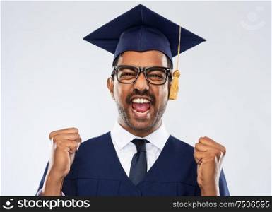 education, graduation and people concept - happy smiling indian male graduate student in mortar board and bachelor gown celebrating success over grey background. happy indian graduate student celebrating success