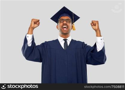education, graduation and people concept - happy smiling indian male graduate student in mortar board and bachelor gown celebrating success over grey background. happy indian graduate student celebrating success