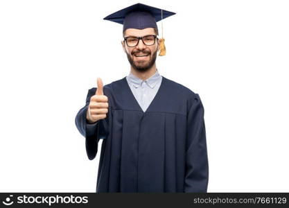 education, graduation and people concept - happy smiling male graduate student in mortar board and bachelor gown showing thumbs up over grey background. happy male graduate student showing thumbs up