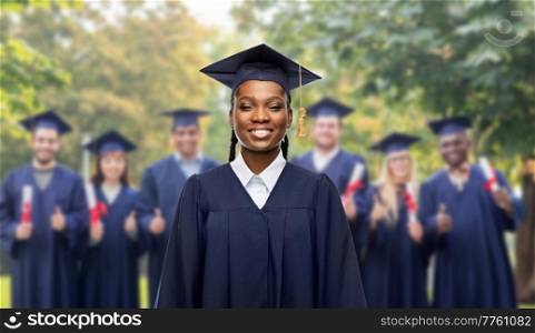 education, graduation and people concept - portrait of happy graduate student woman in mortarboard and bachelor gown over group of people on background. happy female graduate student in mortarboard