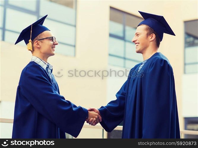 education, graduation and people concept - smiling students in mortarboards and gowns shaking hands outdoors