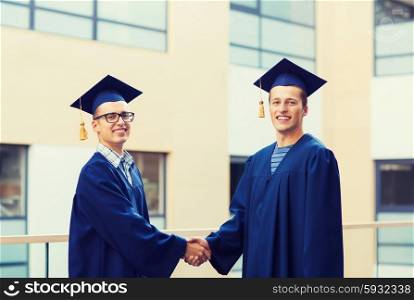 education, graduation and people concept - smiling students in mortarboards and gowns shaking hands outdoors