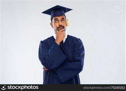 education, graduation and people concept - thinking indian male graduate student in mortar board and bachelor gown over grey background. graduate student in mortar board thinking