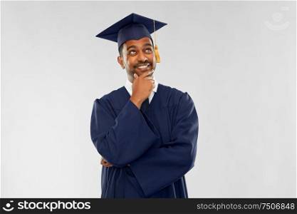 education, graduation and people concept - thinking indian male graduate student in mortar board and bachelor gown over grey background. indian graduate student in mortar board thinking