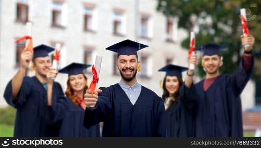education, graduation and school concept - happy smiling male graduate student in mortar board and bachelor gown with diploma over group of people on c&us background. male graduate student in mortar board with diploma