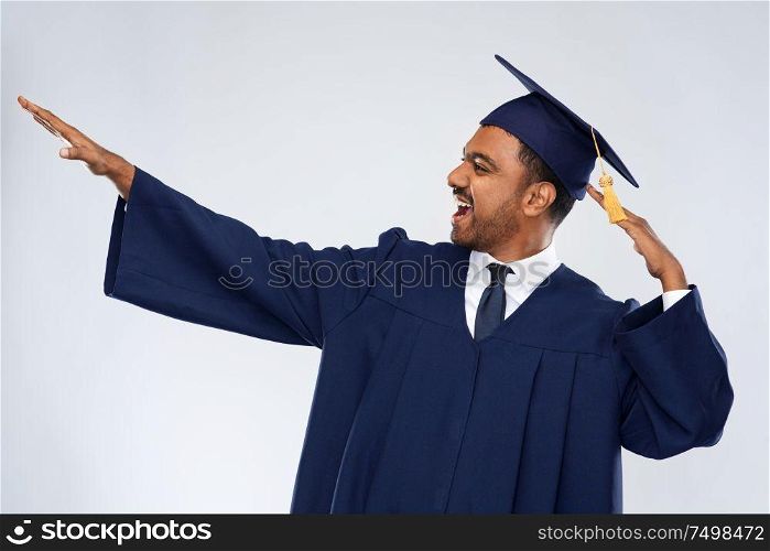 education, graduation and success concept - happy smiling indian male graduate student in mortar board and bachelor gown celebrating success over grey background. happy indian graduate student celebrating success