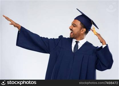 education, graduation and success concept - happy smiling indian male graduate student in mortar board and bachelor gown celebrating success over grey background. happy indian graduate student celebrating success