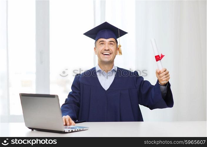education, graduation, business, technology and people concept - happy adult student in mortarboard with diploma and laptop computer sitting at table home or office