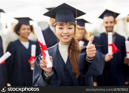 education, graduation, gesture and people concept - group of happy international students in mortar boards and bachelor gowns with diplomas showing thumbs up