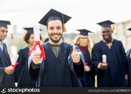 education, graduation, gesture and people concept - group of happy international students in mortar boards and bachelor gowns with diplomas showing thumbs up