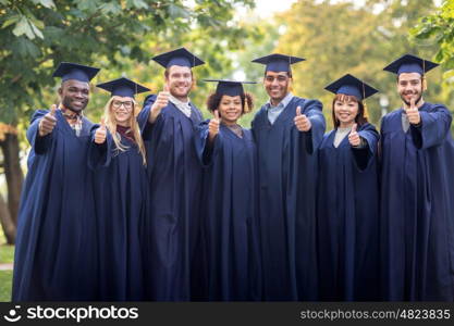 education, graduation, gesture and people concept - group of happy international students in mortar boards and bachelor gowns showing thumbs up