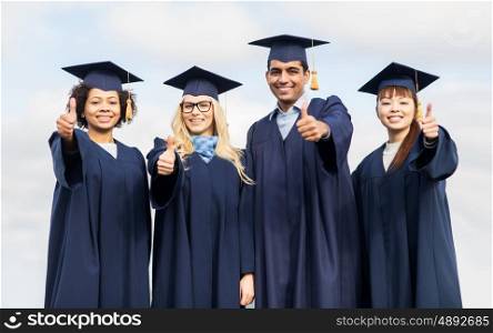 education, graduation, gesture and people concept - group of happy international students in mortar boards and bachelor gowns outdoors showing thumbs up