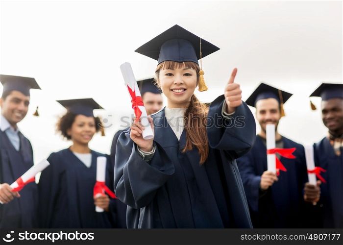education, graduation, gesture and people concept - group of happy international students in mortar boards and bachelor gowns with diplomas showing thumbs up. happy students with diplomas showing thumbs up