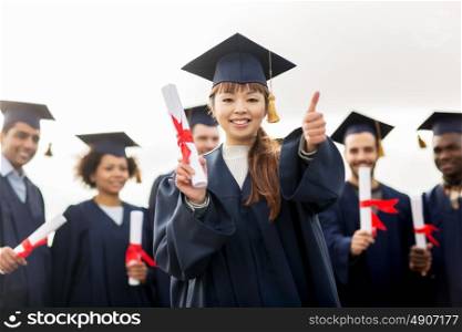 education, graduation, gesture and people concept - group of happy international students in mortar boards and bachelor gowns with diplomas showing thumbs up. happy students with diplomas showing thumbs up
