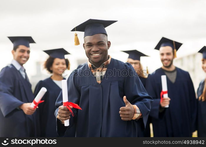 education, graduation, gesture and people concept - group of happy international students in mortar boards and bachelor gowns with diplomas showing thumbs up. happy students with diplomas showing thumbs up