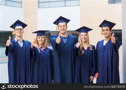 education, graduation, gesture and people concept - group of smiling students in mortarboards and gowns showing thumbs up outdoors