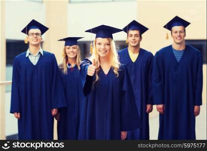 education, graduation, gesture and people concept - group of smiling students in mortarboards and gowns showing thumbs up outdoors