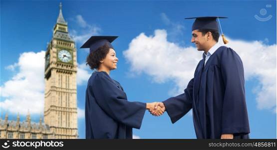 education, graduation, gesture and people concept - happy international students in mortar boards and bachelor gowns greeting each other by handshake over big ben tower and blue sky background