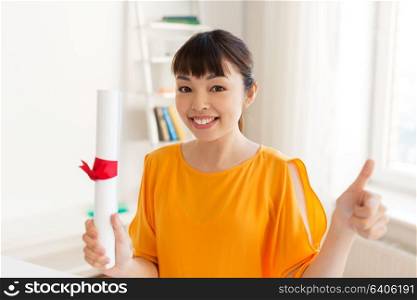 education, graduation, gesture and people concept - smiling student girl in with diploma showing thumbs up at home. happy student girl with diploma showing thumbs up