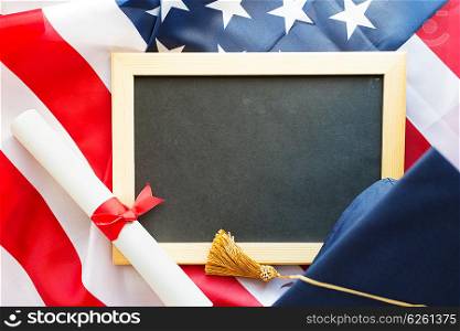 education, graduation, patriotism and nationalism concept - close up of bachelor hat, blackboard and diploma on american flag