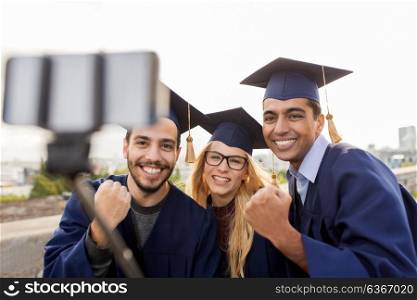 education, graduation, technology and achievement concept - group of happy international students in mortar boards and bachelor gowns taking selfie by smartphone outdoors and celebrating success. happy students or graduates taking selfie outdoors