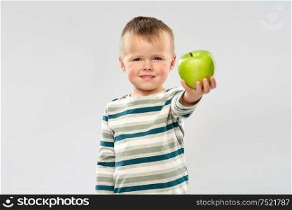 education, health and childhood concept - portrait of smiling little boy holding green apple over grey background. portrait of smiling boy holding green apple