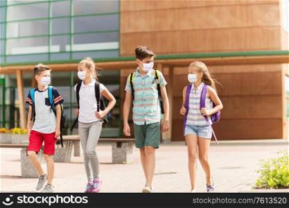 education, healthcare and pandemic concept - group of elementary school students wearing face protective medical masks for protection from virus disease with backpacks walking and talking outdoors. group of school students in masks leaving school