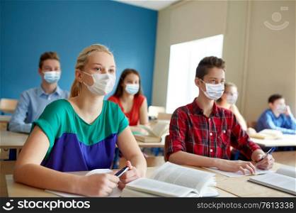 education, healthcare and pandemic concept - group of students wearing face protective medical mask for protection from virus disease with books at school lesson. group of students in masks at school lesson